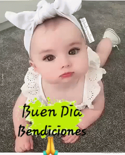 A Baby Girl Wearing A White Headband And A White Dress Is Laying On The Floor . GIF