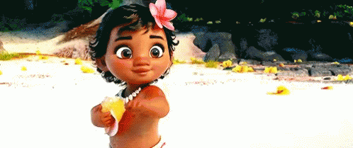 A Baby Girl With A Flower In Her Hair Is Standing On A Beach Holding A Shell . GIF