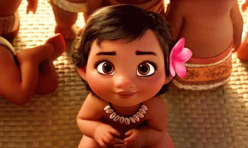 A Baby Girl With A Pink Flower In Her Hair Is Sitting On A Mat . GIF