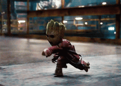 A Baby Groot Is Running Down A Street Wearing Sunglasses And A Red Jacket GIF