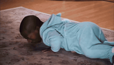A Baby In A Blue Pajamas Is Doing Push Ups On A Rug GIF