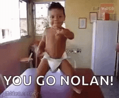 A Baby In A Diaper Is Pointing At The Camera While Standing On A Purple Balloon . GIF