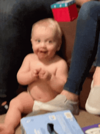 A Baby In A Diaper Is Sitting On The Floor Next To A Box That Says ' Socks ' On It GIF