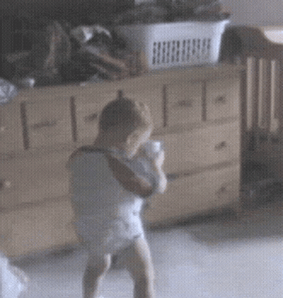 A Baby In A Diaper Is Standing In Front Of A Dresser With A Basket In The Background GIF