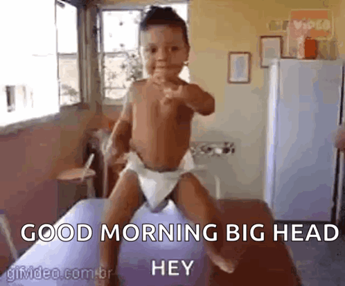 A Baby In A Diaper Is Standing On A Bed With The Words `` Good Morning Big Head Hey '' . GIF