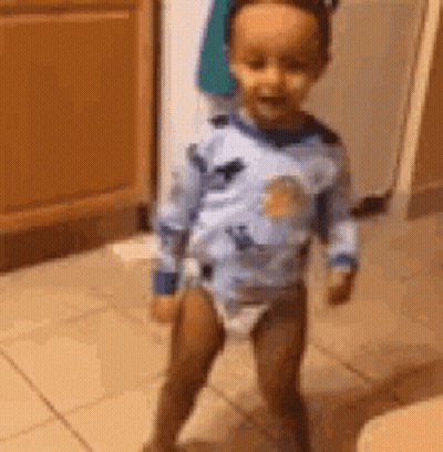 A Baby In A Diaper Is Standing On A Tiled Floor In A Room . GIF