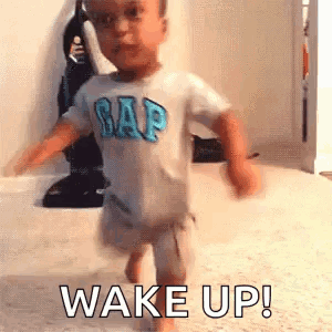A Baby In A Gap Shirt Is Walking On The Floor And Says `` Wake Up '' . GIF