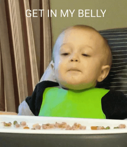 A Baby In A High Chair With A Plate Of Food And The Words Get In My Belly Above Him GIF