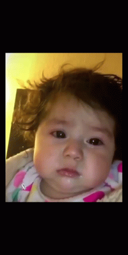 A Baby In A Pink And White Polka Dot Outfit Is Looking At The Camera GIF