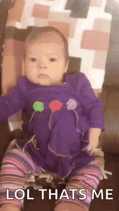 A Baby In A Purple Dress Is Sitting On A Couch And Making A Face . GIF