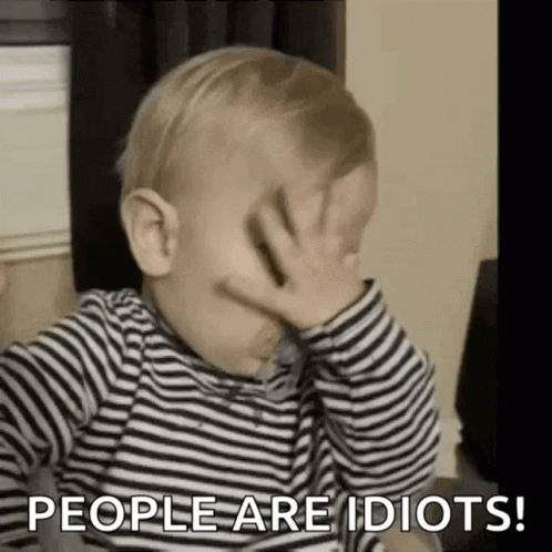 A Baby In A Striped Shirt Is Covering His Face With His Hand . GIF