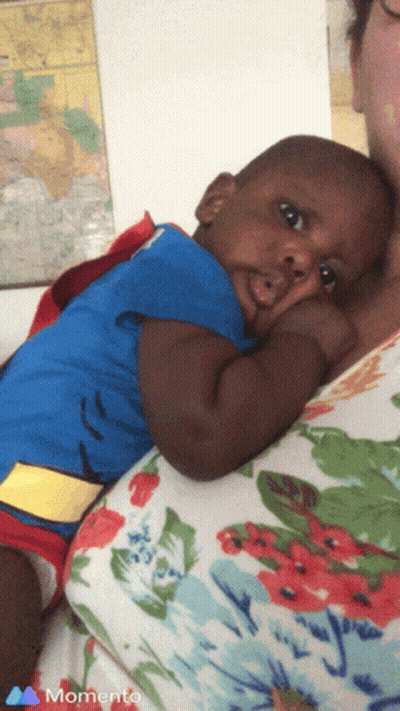 A Baby In A Superman Costume Is Being Held By A Woman In A Momento Photo GIF