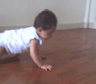 A Baby In A White Dress Is Crawling On A Wooden Floor . GIF