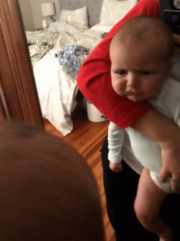 A Baby Is Being Held By A Person In Front Of A Messy Bed GIF