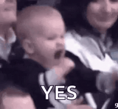 A Baby Is Being Held By A Woman In A Crowd And Making A Funny Face . GIF