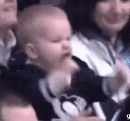 A Baby Is Being Held In A Woman 'S Arms While Sitting In A Crowd . GIF