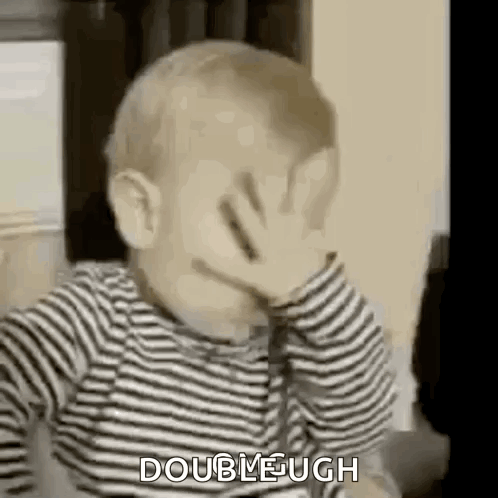 A Baby Is Covering His Face With His Hand While Wearing A Striped Shirt . GIF