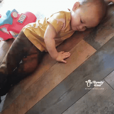 A Baby Is Crawling On A Wooden Floor Next To A Toy Car With The Number 2123 On It GIF