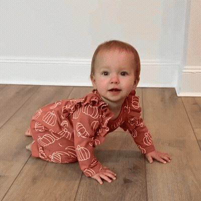 A Baby Is Crawling On A Wooden Floor Wearing A Pink Outfit With Pumpkins On It GIF