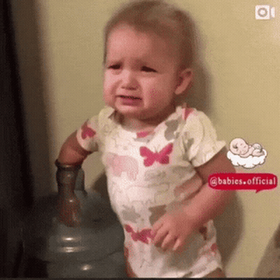 A Baby Is Crying In Front Of A Water Bottle . GIF