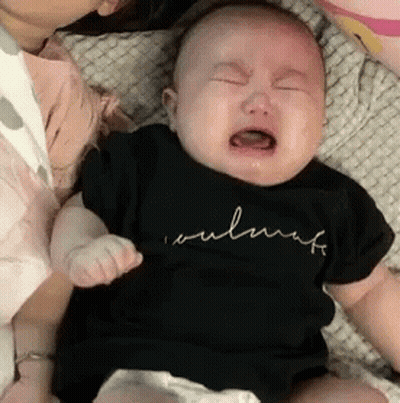A Baby Is Crying While Being Held By A Woman And Wearing A Black Shirt . GIF