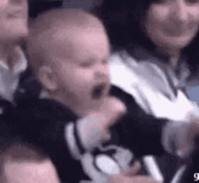 A Baby Is Crying While Being Held By A Woman In A Crowd . GIF