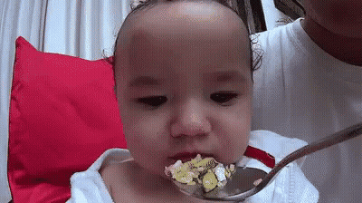 A Baby Is Eating From A Spoon With A Spoon In His Mouth . GIF