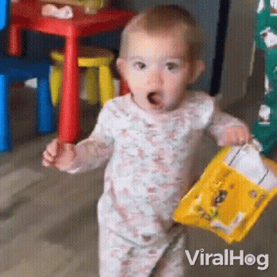 A Baby Is Holding A Bag Of Chips In Her Hands . GIF