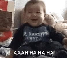 A Baby Is Laughing While Sitting On A Bed With Boxes In The Background . GIF