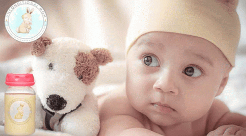 A Baby Is Laying Next To A Stuffed Dog And A Bottle Of Breast Milk GIF