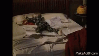 A Baby Is Laying On A Bed With A Cake On The Nightstand . GIF