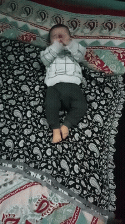 A Baby Is Laying On A Bed With A Paisley Patterned Blanket GIF