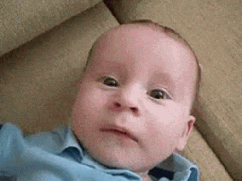 A Baby Is Laying On A Couch And Looking At The Camera . GIF