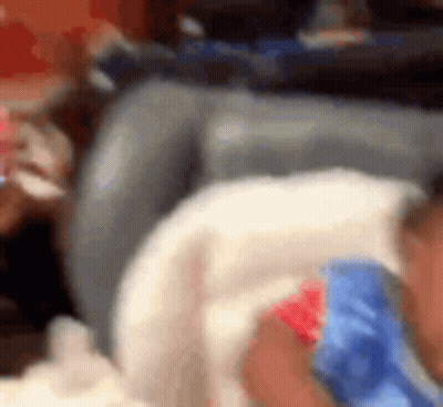 A Baby Is Laying On A Couch Wearing A Blue And Red Shirt . GIF
