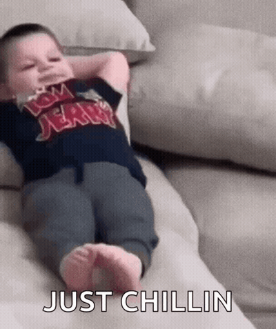 A Baby Is Laying On A Couch With His Arms Over His Head And The Words `` Just Chillin '' Written On The Bottom . GIF