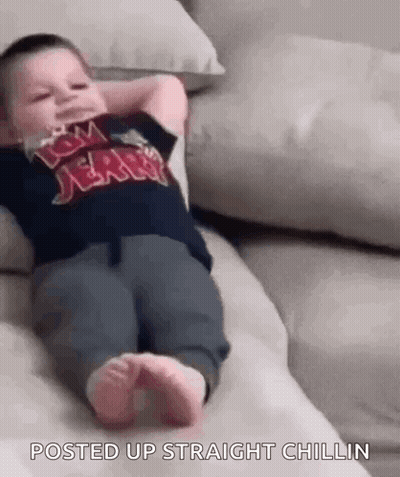 A Baby Is Laying On A Couch With His Hands Behind His Head And His Feet Up . GIF