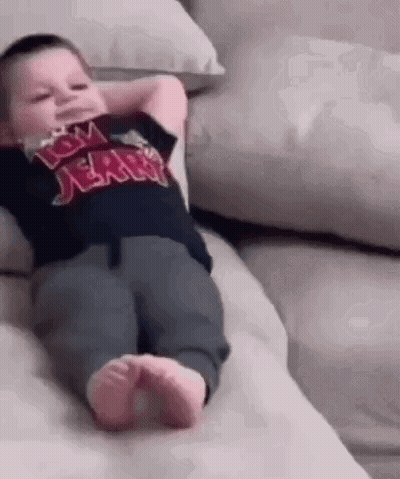 A Baby Is Laying On A Couch With His Hands Behind His Head And Wearing A Tom And Jerry Shirt . GIF