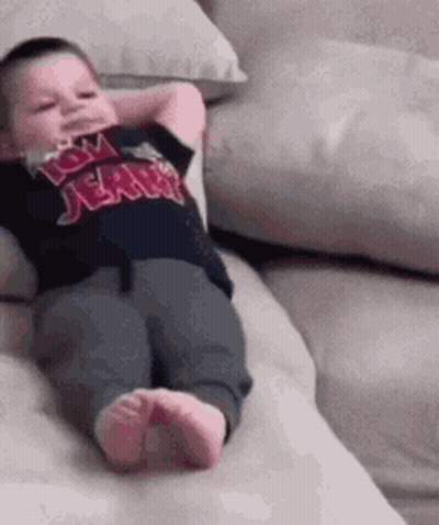 A Baby Is Laying On A Couch With His Hands Behind His Head And Wearing A Tom Jerry Shirt . GIF