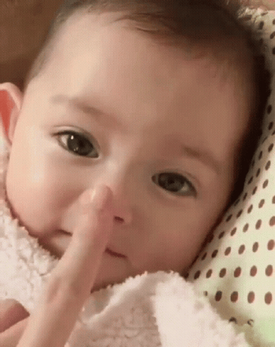 A Baby Is Laying On A Polka Dot Pillow And Touching His Nose . GIF