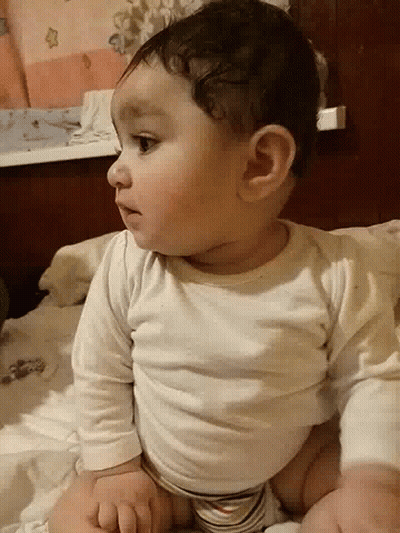A Baby Is Laying On His Stomach On A Bed GIF