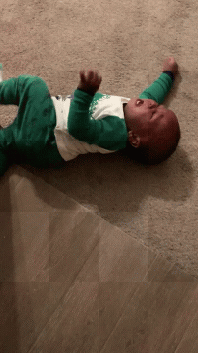 A Baby Is Laying On The Floor Crying And Wearing A Shirt That Says ' Christmas ' On It GIF
