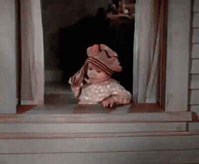 A Baby Is Looking Out Of A Window Wearing A Hat And Holding A Towel . GIF