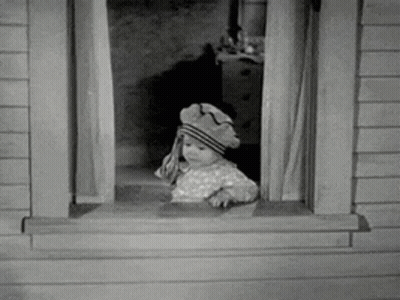 A Baby Is Looking Out Of A Window Wearing A Hat . GIF