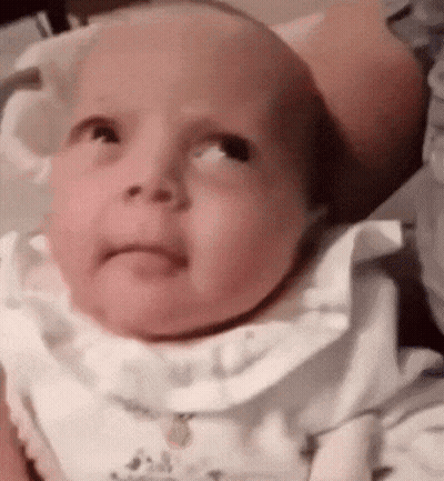 A Baby Is Looking Up At The Camera While Wearing A White Shirt And Bib . GIF