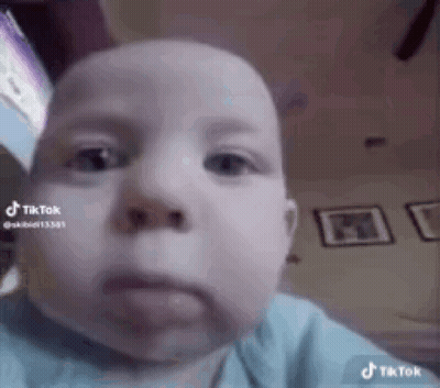 A Baby Is Making A Funny Face While Looking At The Camera In A Living Room . GIF