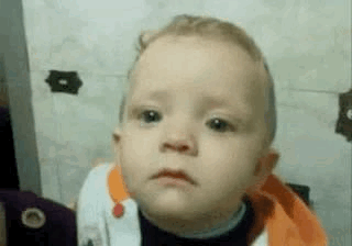 A Baby Is Making A Sad Face In Front Of A Wall . GIF