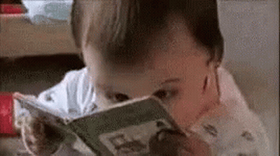 A Baby Is Reading A Book While Sitting On A Table . GIF