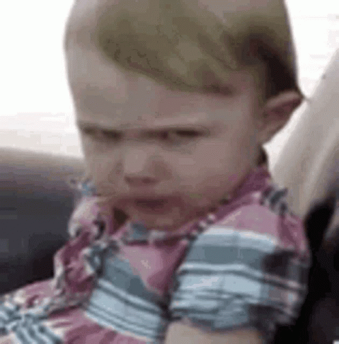 A Baby Is Sitting In A Car Seat And Making An Angry Face . GIF