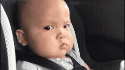 A Baby Is Sitting In A Car Seat With A Seat Belt On Making A Funny Face . GIF