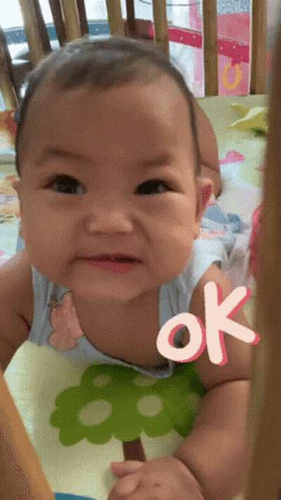 A Baby Is Sitting In A Crib With An Ok Sticker On His Chest GIF